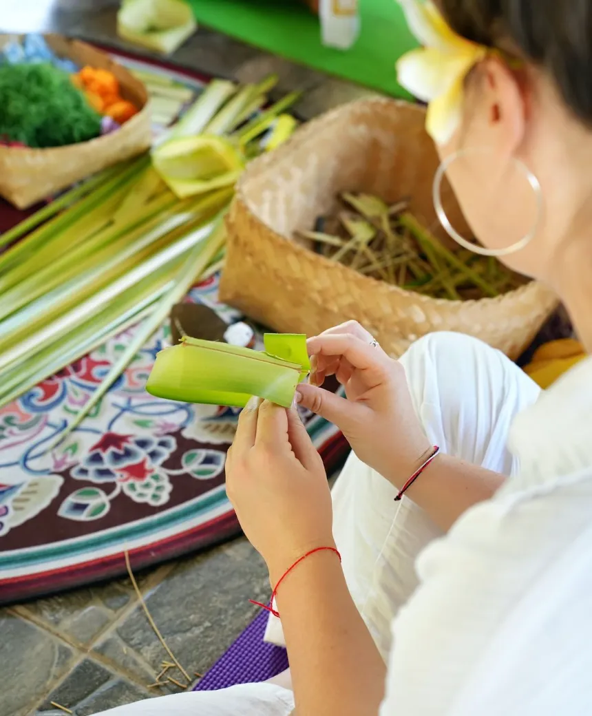 Hands carefully arranging flowers inside a canang sari